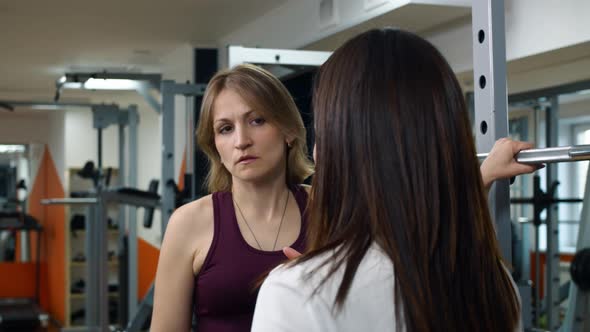 Two Women in the Gym are Talking to Each Other Discussing Sports Exercises to Improve the Muscular