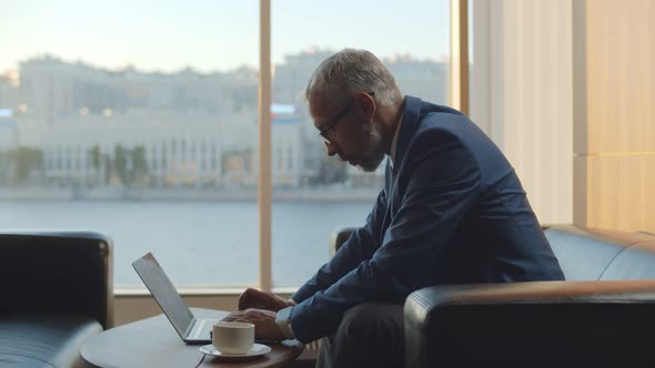 Business Executive Sitting on Couch at Business Center Lobby Working on Laptop and Drinking Coffee