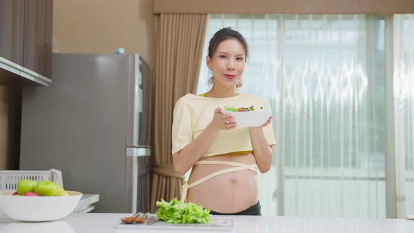 Portrait of Asian young pregnant woman hold salad in bowl in kitchen.