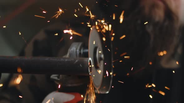 Male Repairman Cuts Metal Pipe From Which Sparks Fly with Help of an Angle Grinder Closeup