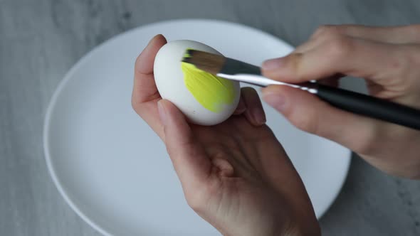 Close-up. Female hands paint Easter egg in a modern minimalist style with colorful paint.