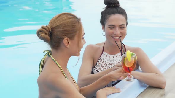 Two Gorgeous Women Talking and Drinking Cocktails at the Swimming Pool