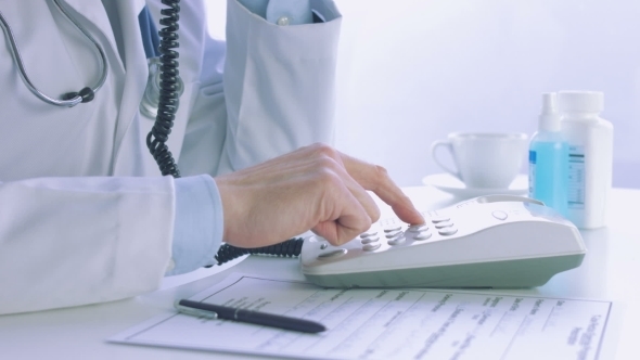 Male Doctor Dialing a Phone In a Medical Office