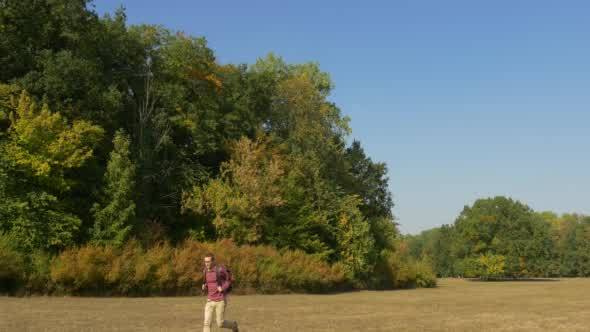 Man With Backpack Runs On The Lawn With Dry Grass