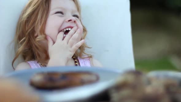 Pre-schooler at lunch in backyard with family, laughing and enjoying her food.