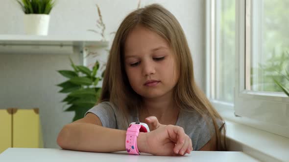 Serious Caucasian Little Girl Clicks on the Screen of Kids Smartwatch