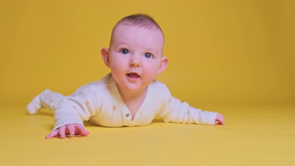 Happy infant baby boy laughing lying on his tummy, yellow studio background