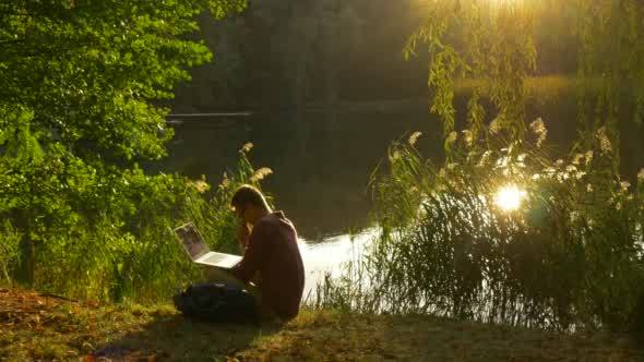 Man Sits On The Ground At The Lakeshore He Takes