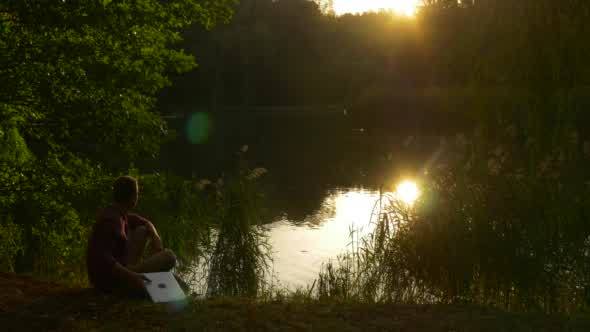 Man Sits On The Ground And Looks At The Lake
