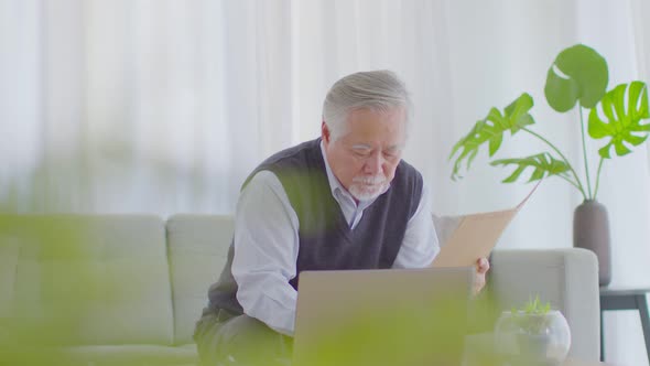 Asian senior handsome business man with white hairs hold book and learning with computer laptop