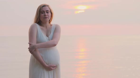 A Young Pregnant Woman Stands Near the Sea Where the Sun Sets