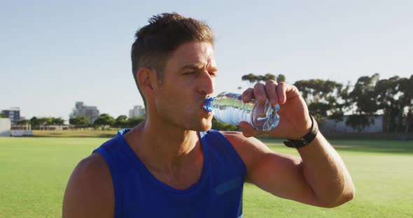 Fit caucasian man exercising outdoors, resting, drinking water