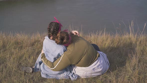Women Hug Having Date on Steep Bank of River in Evening