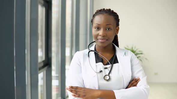 Young African Woman Doctor or Nurse Standing in Medical Suit at Clinic and Looking at Camera