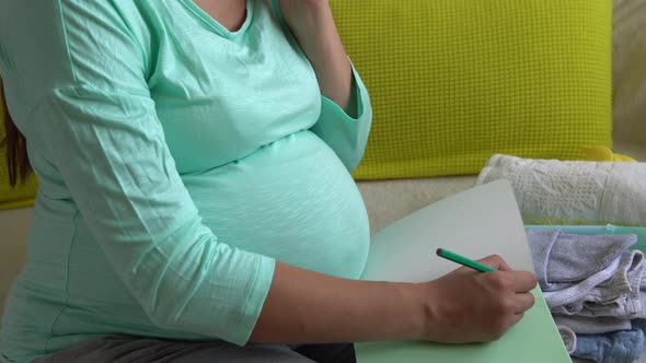 Cute Pregnant Woman Writing Packing List for Maternity Hospital With Notebook Prepares Bags