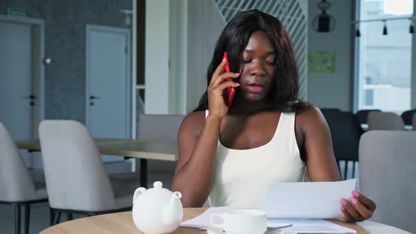 AfricanAmerican Woman with Papers Talks on Phone in Cafe