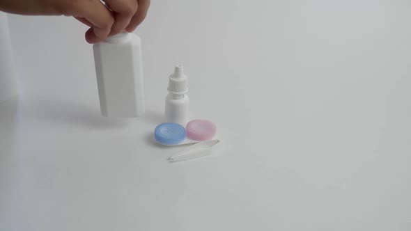 A Woman's Hand Places a Bottle of Lens Cleaning Solution on a White Table