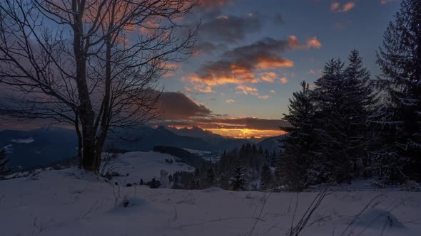 idyllic sunset in a snowy landscape with moving colorful clouds, trees and a snowman