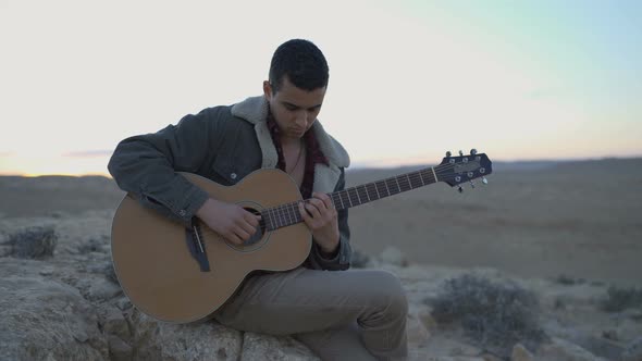 Cool young man playing guitar on a desert mountain