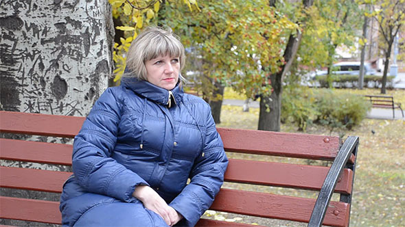 A Young Woman Sits on a Bench in a City Park