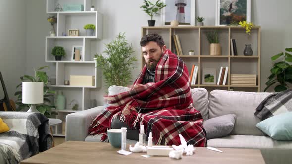 Ill Man with Chills and Wraps Himself in a Blanket on the Sofa in Living Room