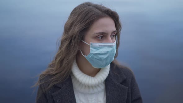 Closeup Portrait of Young Brunette Woman in Covid19 Face Mask with River Water at Background