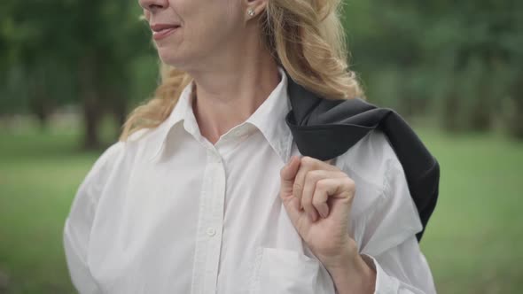 Closeup of Unrecognizable Smiling Middle Aged Woman with Jacket on Shoulder Walking Outdoors on