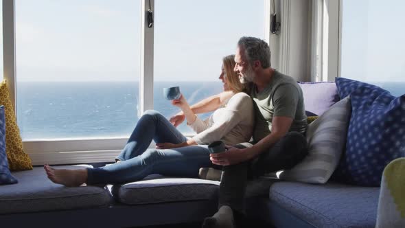 Happy caucasian mature couple drinking coffee and talking in sunny living room