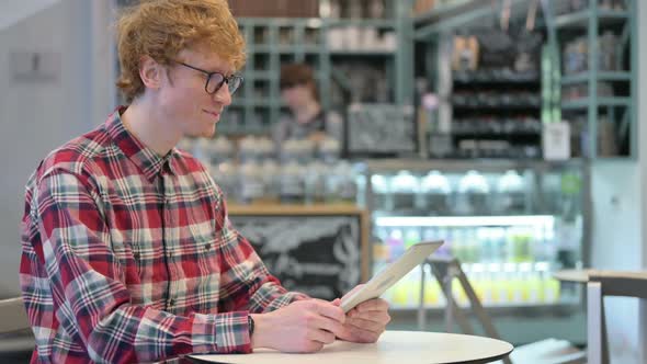 Online Video Chat on Tablet By Young Redhead Man in Cafe