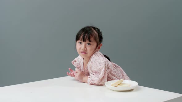 Asiatic child eating piece of sweet in studio with gray background.