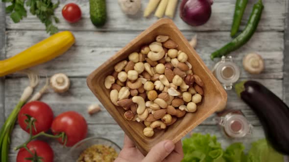 Cook Placing Wooden Bowl of Nuts on Table with Various Ingredients