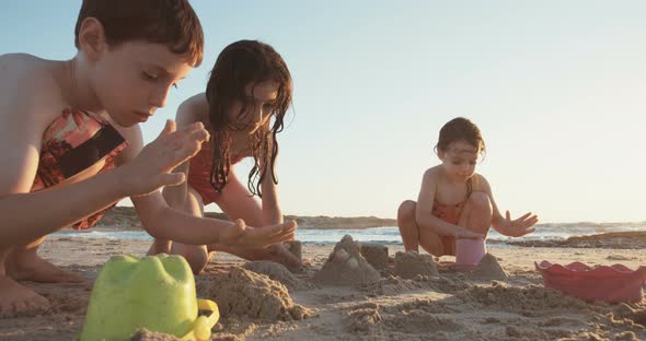 Three kids playing on the beach building sand castles together