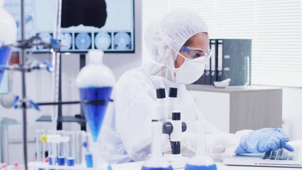 Female Scientist Typing Formula on Laptop and Looking Through Microscope in Modern Science alt