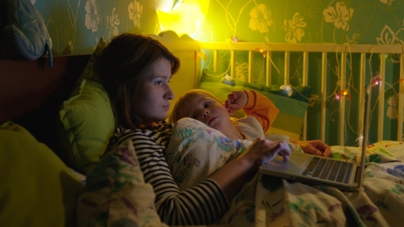 Mother And Son Lying In Bed With Laptop