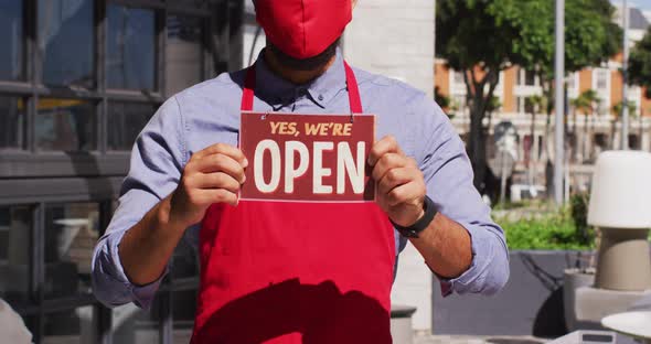 Mixed race male cafe worker wearing face mask showing were open signage