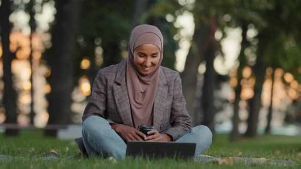 Happy Cheerful Muslim Girl in Hijab Business Woman Sitting on Green Grass Lawn Park Using Laptop for