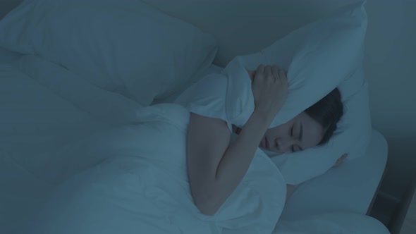 Asian young woman with upset and angry feel due to noise and put cozy blanket on her ears at night.