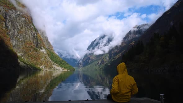 Beautiful fjord landscape at Sognefjord of Norway. Man in yellow raincoat sitting at the edge of a q