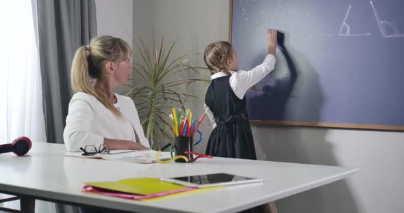 Diligent Caucasian Schoolgirl Turning To Blackboard and Writing with Chalk