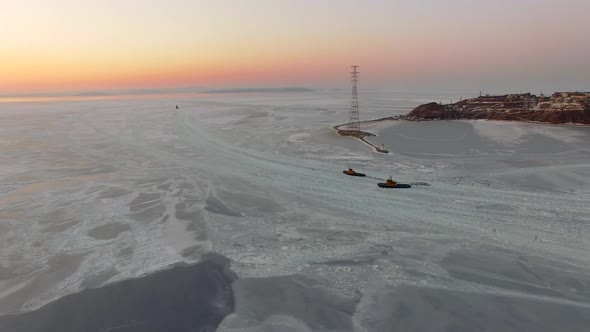 Drone View of the Ice-bound Strait with Two Tugboats Operating at Sunset