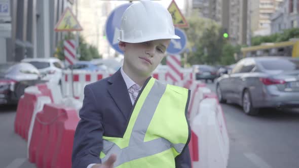 Tired Little Boy in Constructor Helmet on His Head, and Uniform Looking in Camera Showing Thumb Up