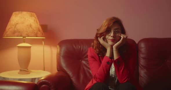 Beautiful girl with red jacket and glasses is bored sitting on the sofa at home