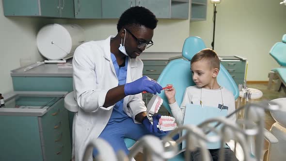 African Young Dentist Teaching Little Boy How to Brush Teeth on the Plastic Model