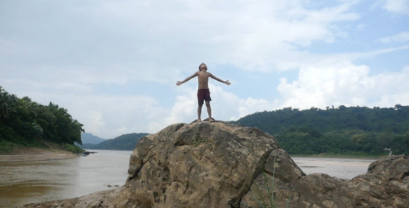 Kid Standing With Arms Outstretched On The Rock
