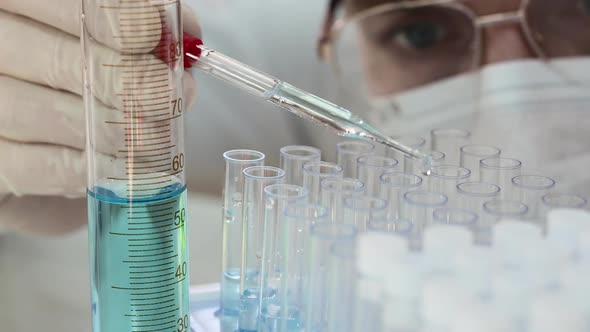 Scientist in Mask and Eyeglasses Dripping Liquid Into Test Tube. Close Up