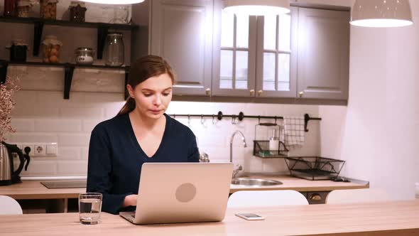 Woman Celebrating Online Success While Working on Laptop in Kitchen