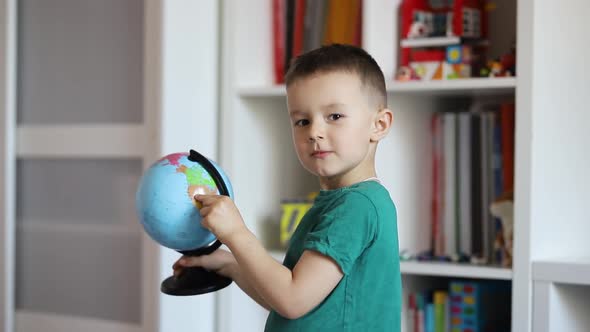 Little boy with a globe in his hands shows thumb up