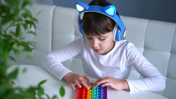 Baby Girl Playing with Rainbow Pop It Fidget and Listening Music with Headphones