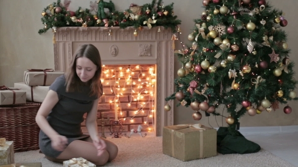 Young Woman Is Putting Gifts Under Christmas Tree