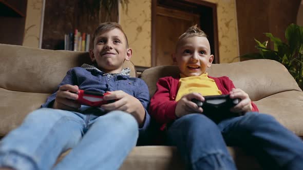 Brothers Sitting on Cozy Sofa at Home and Celebrating Victory in Video Game